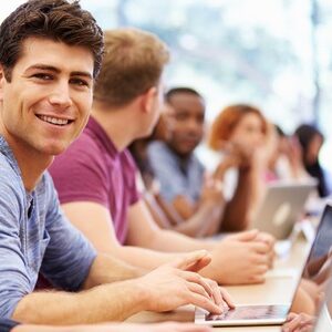 Ausbildungsgruppe sitzend vor Laptops. Ein Auszubildender lächelt in die Kamera